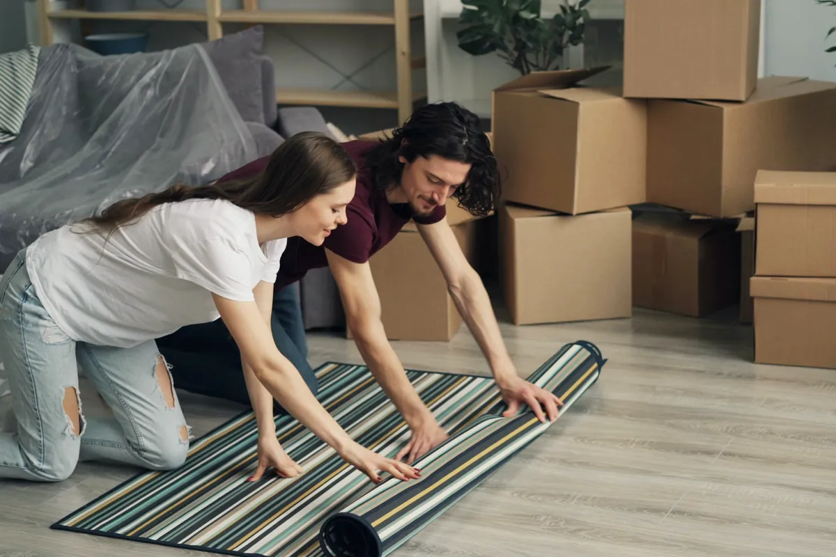 Couple setting up their new home, unrolling a rug among moving boxes